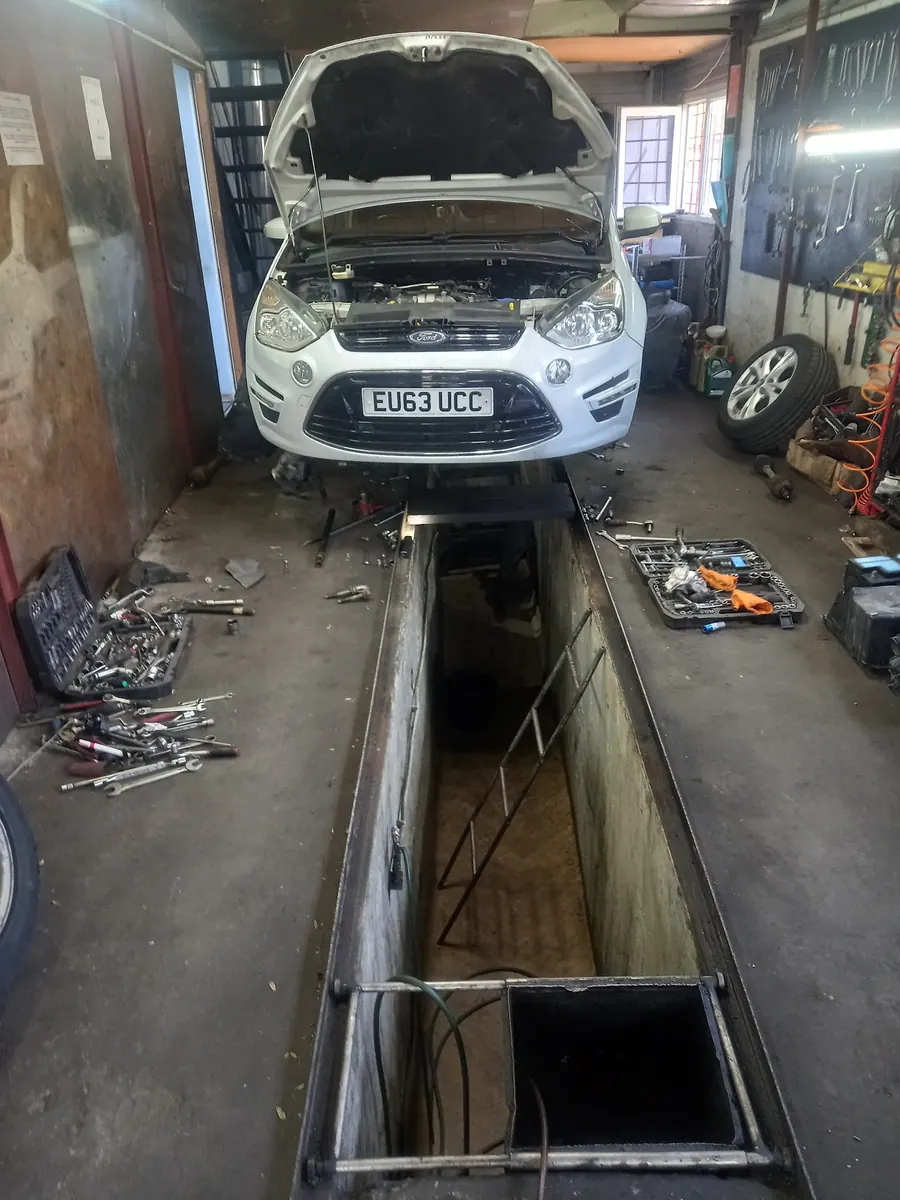 Autoturism ridicat pe elevator deasupra gropii de vizitare, cu capota deschisă